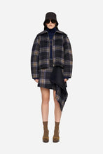 Person wearing a plaid reversible jacket, matching skirt, and brown boots on a light grey background