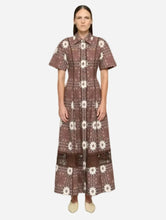 A woman stands against a light gray studio background wearing a short-sleeved t-shirt midi dress with a brown and white floral pattern and a pointed collar.