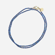 Blue beaded necklace with a gold clasp on a light grey background