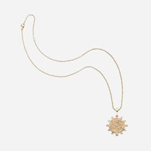 A gold chain necklace featuring a circular, textured pendant adorned with small multicolored gemstones, displayed on a clean white background.