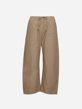 A pair of wide-leg pants in a light tan color, featuring an elastic waistband with a drawstring, shown against a plain light gray background.