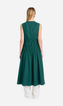 Woman in green sleeveless dress seen in back view on a light gray background