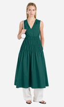 Woman wearing a green dress with white pants on a plain background