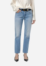 A model wearing a light-wash blue straight-leg jeans with a black belt, and black pointed-toe heels, photographed against a light gray studio background.