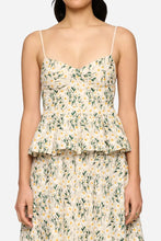 Woman wearing a floral tank top that flares at the bottom on a light grey background