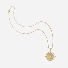 A gold chain necklace featuring a circular pendant with small clear stones around the edge, displayed on a light grey background.