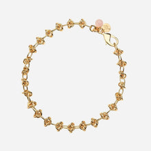 A gold chain necklace with a repeating interlocking knot pattern and a small pink rose quartz bead charm, shown on a light grey background.