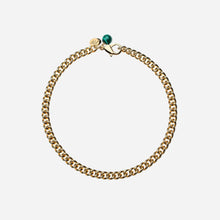 Gold chain bracelet with a green bead on a light grey background