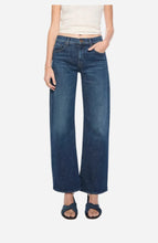 A model wearing a pair of dark blue wide-leg jeans, paired with a cream ribbed tank top and dark blue slide sandals, against a light grey background.