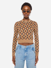 Woman wearing a beige, brown, and yellow diamond patterned sweater and jeans on a light grey background