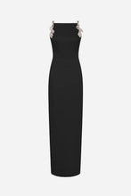 A black sleeveless maxi dress with decorative silver-toned floral embellishments at the shoulders, shown against a light grey background.