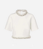 a white crewneck top with beading detail at the color and hem of the shirt. displayed on a light grey background.