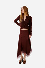 A woman modeling a matching dark brown two-piece outfit consisting of a cropped button-front cardigan and a silk skirt with a lace hem, paired with brown platform sandals, against a plain light gray studio background.