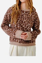 A woman wearing a brown and beige leopard print knit sweater with ribbed cuffs and hem, against a plain light gray background.