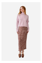 A woman modeling a light pink mock-neck knit sweater and a brown leopard-print midi skirt, paired with brown platform sandals, against a plain light gray studio background.