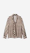 A long-sleeve blouse with a beige and dark green checkered pattern, displayed on a light grey background.