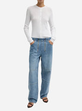 Person wearing a white sweater and blue jeans with two vertical zippers parallel to the front seam and patchwork legs on a light gray background