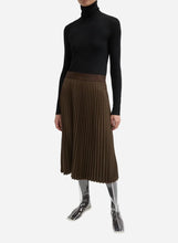 Person wearing a brown pleated midi length skirt on a light grey background