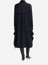 A model shown from the back wearing a long, dark navy blue shirt dra, paired with black knee-high boots against a light gray studio background.