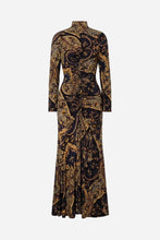 A long-sleeve high-neck maxi dress with a fitted bodice and flared skirt, featuring an intricate gold and black paisley pattern, shown against a light grey background.